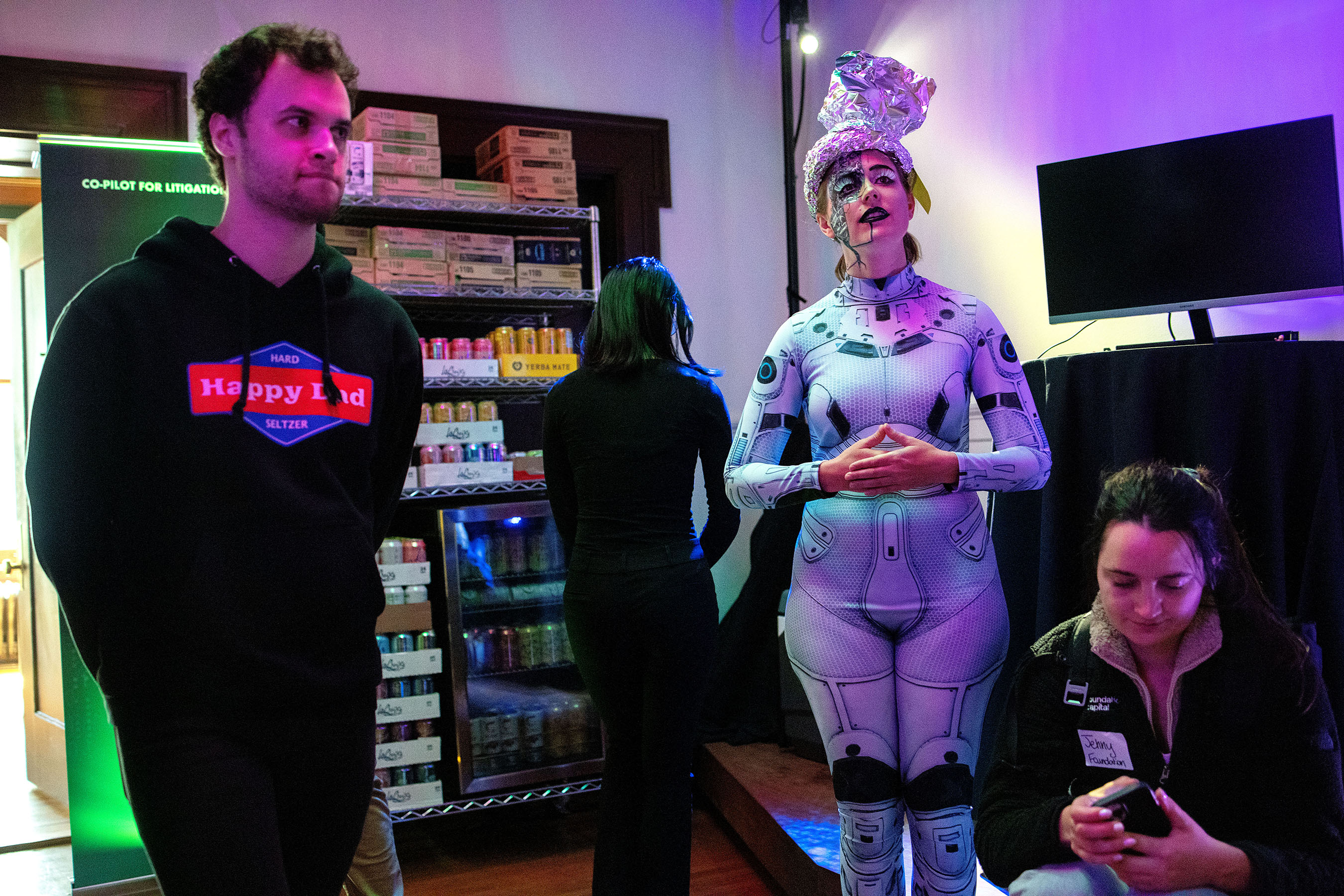 Michaela Carmein (second from right) watches demos while helping out during the HF0 Demo Day where she entertained guests by pretending to be an AI robot named “Guinevere” during the event for the start-up fellowship in San Francisco, Calf., on Tuesday, April 4, 2023. She talked to guests in character throughout the entire event. Carmein’s close friend, Emily Liu, is one of the co-founders of HF0, and she helped her friend create a memorable event with the costume and act. Demo days at other programs can often be routine events with start-ups mostly giving slide deck presentations, but the HF0 team added creative details throughout their demo day to make the event fun for guests.